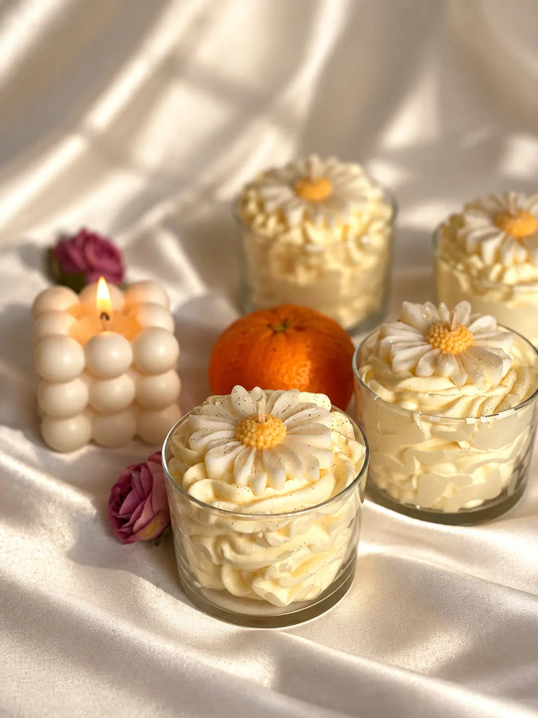 Velas tipo postre con margaritas de cera en vasos de cristal sobre tela clara